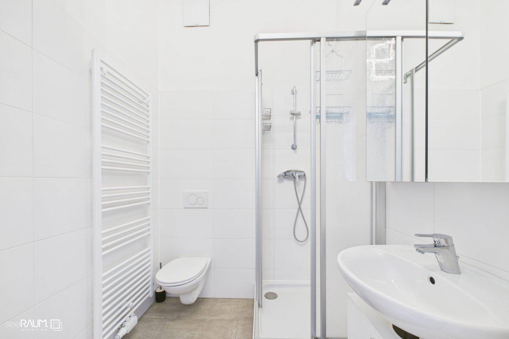 Helles Badezimmer mit Duschkabine, wandhängendem WC und beheiztem Handtuchhalter.