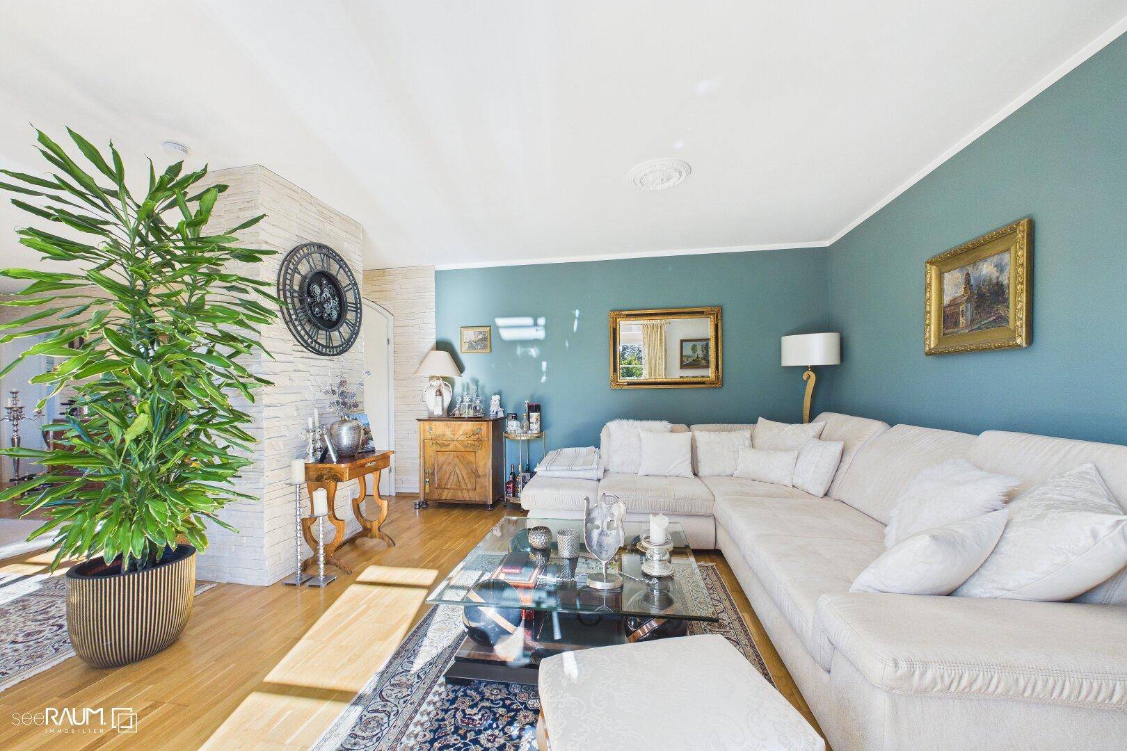 Helles Wohnzimmer mit großem Ecksofa, Holzboden und blauer Akzentwand.