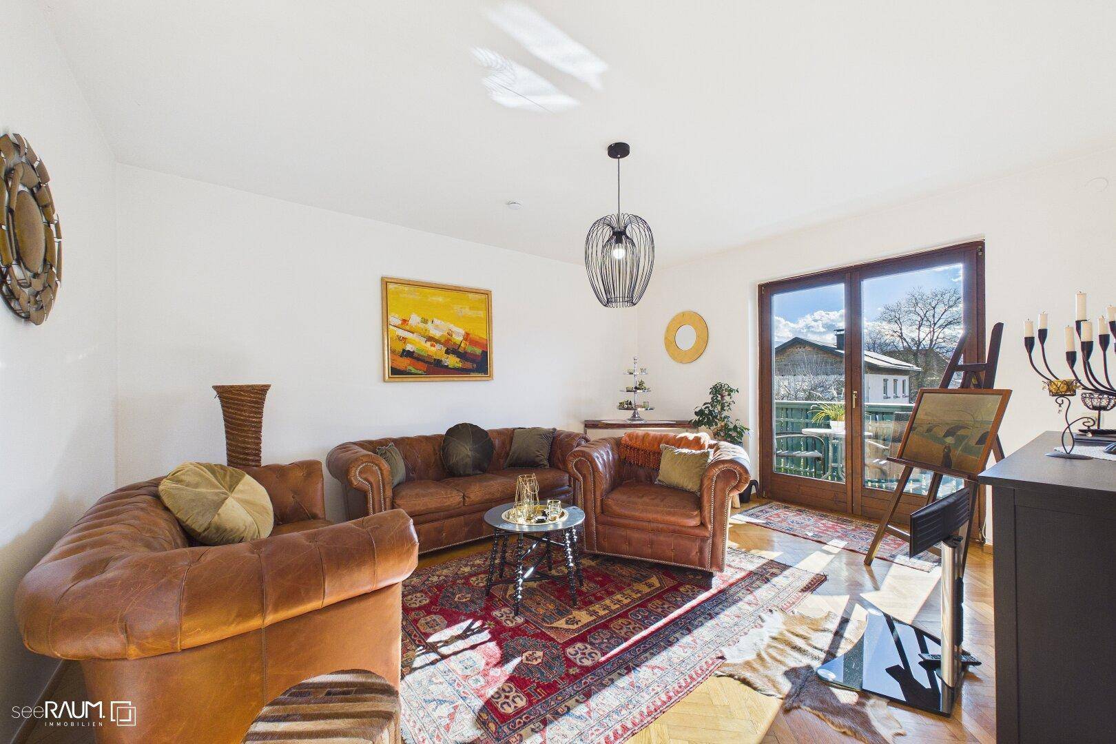 Helles Wohnzimmer mit Ledersofas, Holzboden und Zugang zum Balkon.