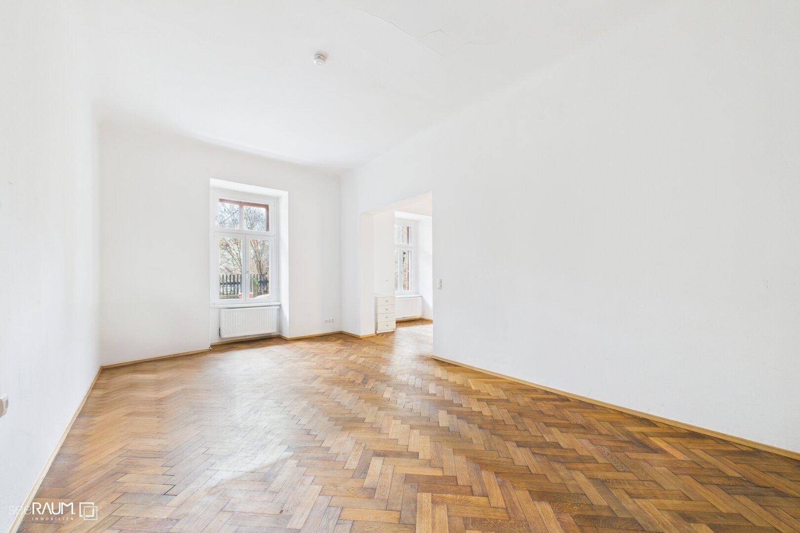 Heller, leerer Raum mit Fischgrätparkett und großem Fenster, ideal für Wohn- oder Schlafzimmer.