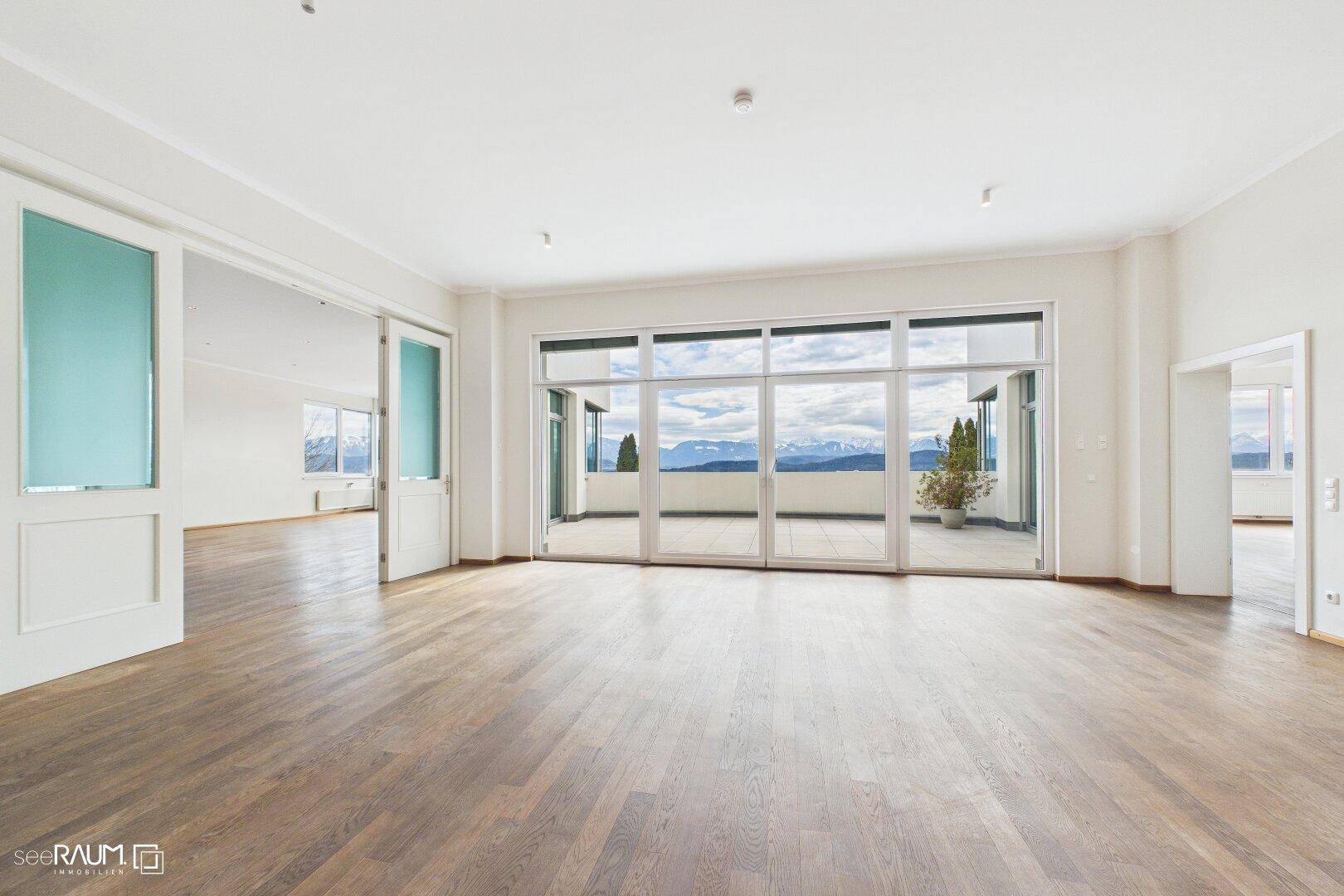 Heller, leerer Raum mit großen Fensterfronten, die einen weiten Blick auf die Berge und die Landschaft bieten.