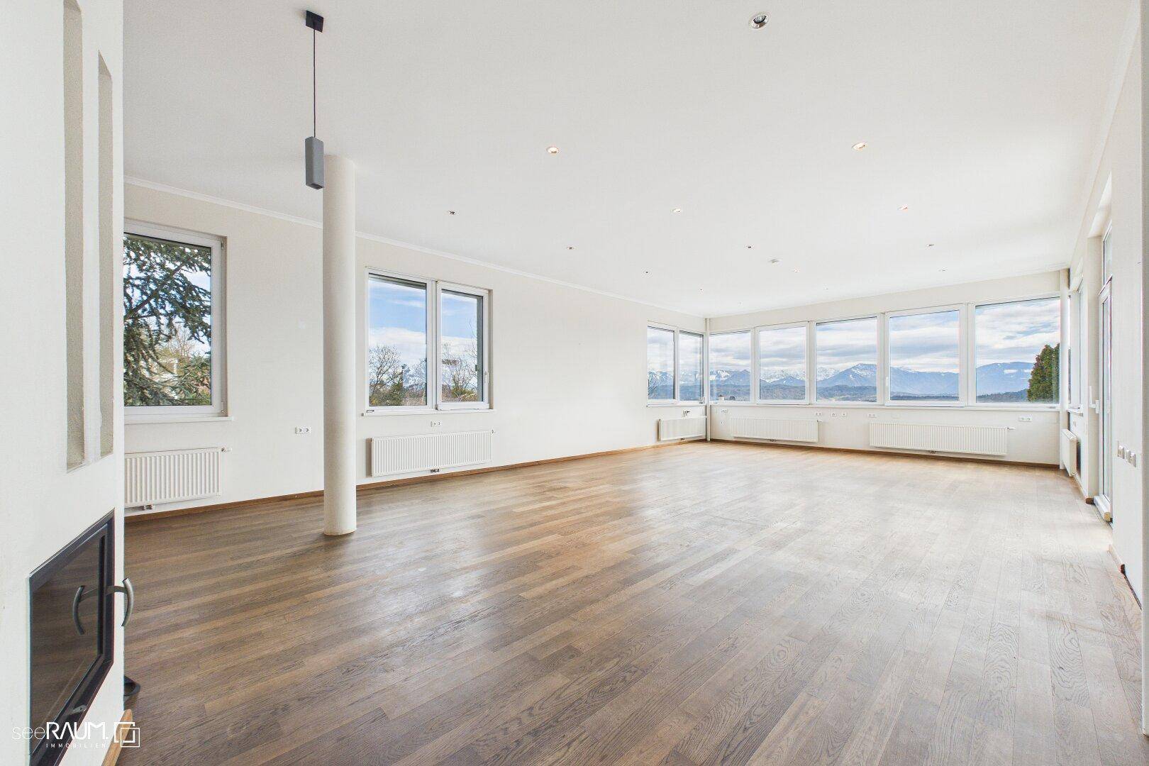 Geräumiges Wohnzimmer mit Parkettboden, Kamin und großen Fenstern, die einen beeindruckenden Bergblick freigeben.