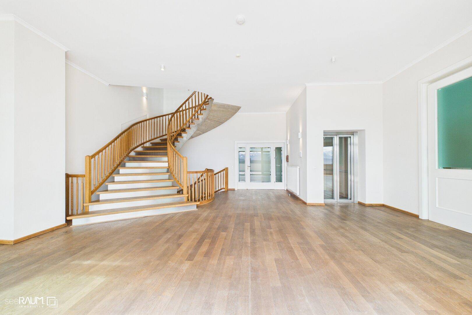 Geräumiger Eingangsbereich mit eleganter Holztreppe, Parkettboden und einem sichtbaren Aufzug.