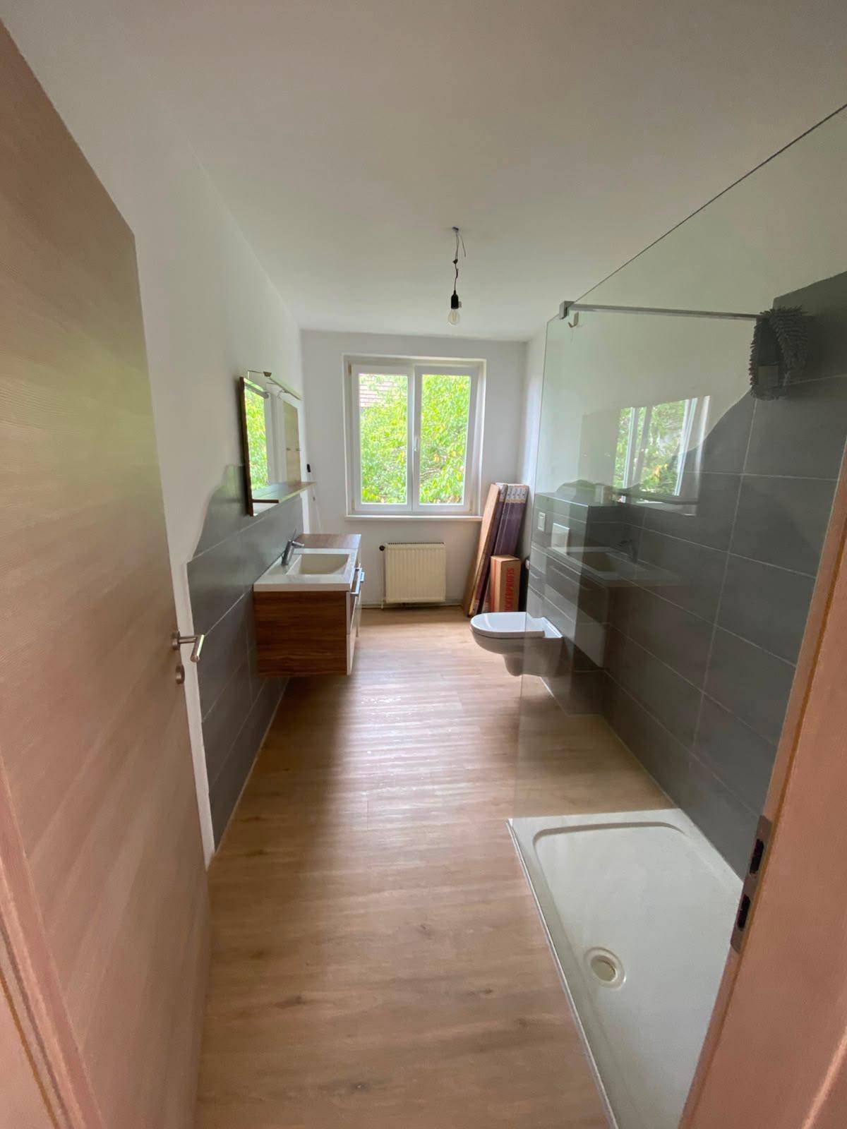 Modernes Badezimmer mit Dusche, Doppelwaschbecken, wandhängendem WC und Fenster für Tageslicht.