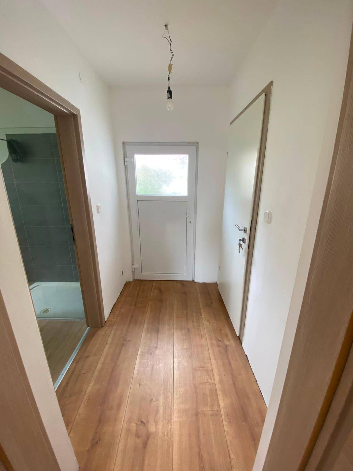 Heller Flur mit Laminatboden und einer Tür, die zu weiteren Räumen führt, sowie einem Fenster am Ende.