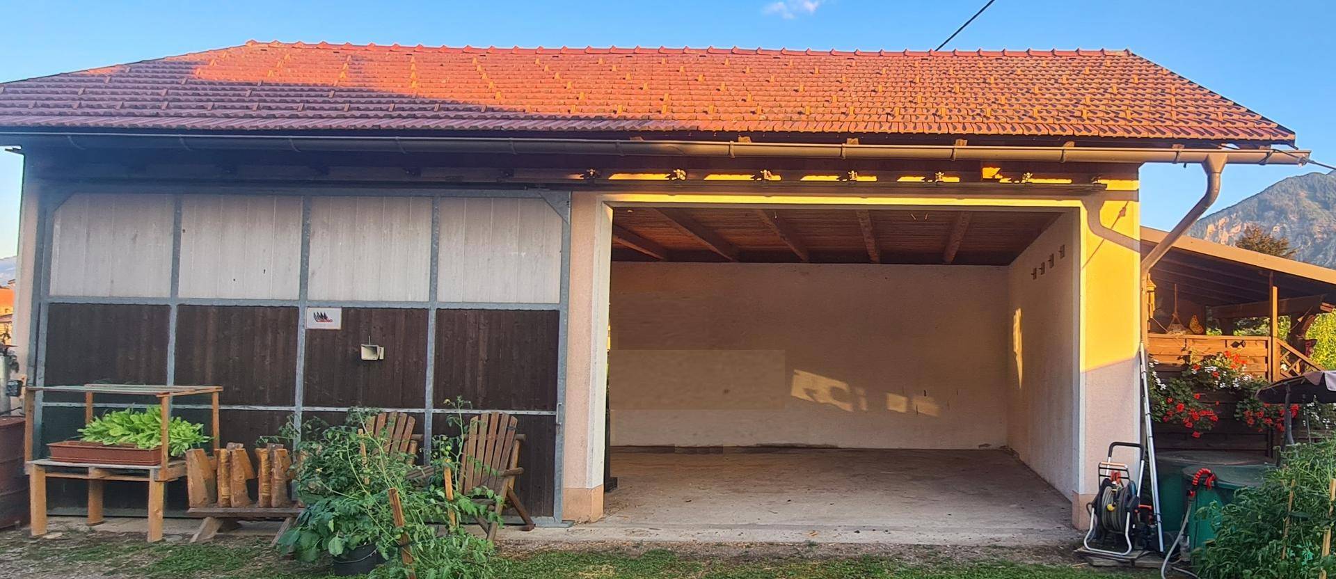 Offenes Garagentor zeigt den Innenraum der Garage, umgeben von einem grünen Garten und Bergen.