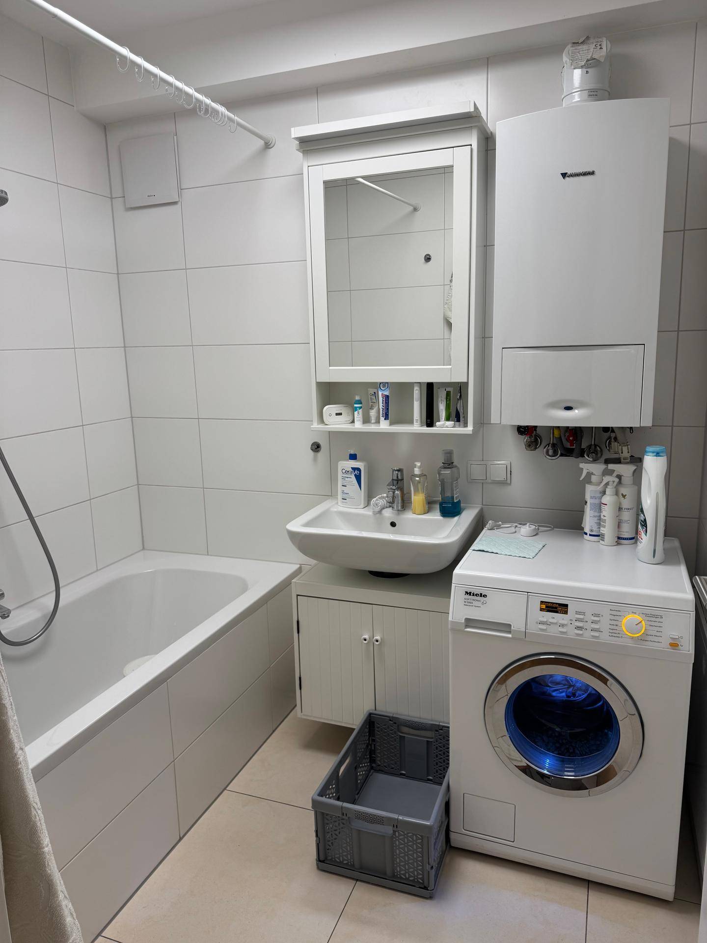 Helles Badezimmer mit Badewanne, Waschbecken, Spiegelschrank und Waschmaschine.