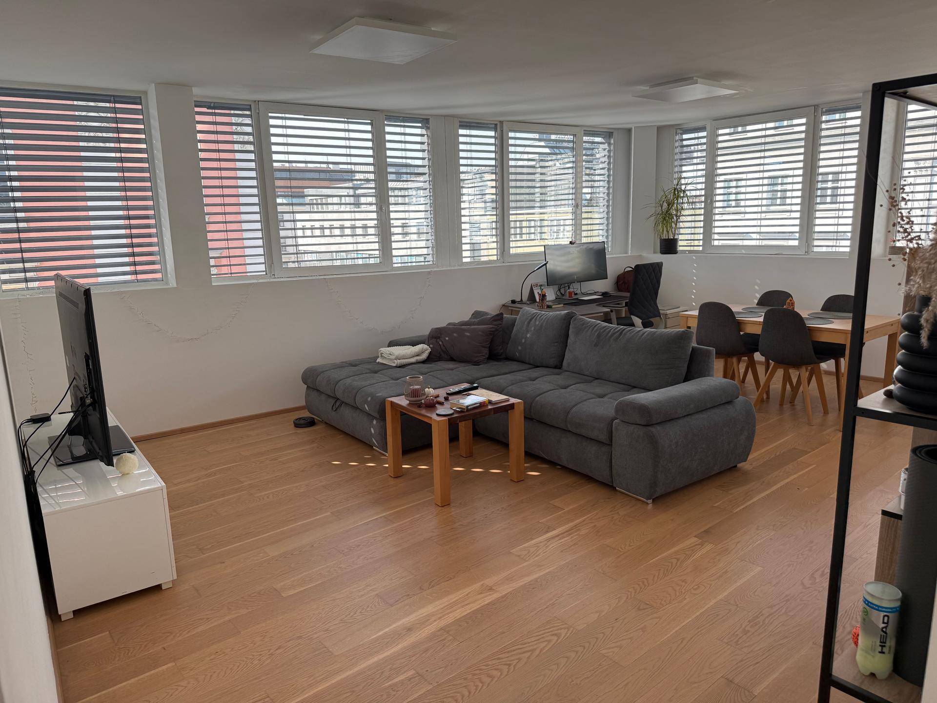 Heller Wohn-Essbereich mit Holzboden, bequemer Couch und Fenstern mit Jalousien.