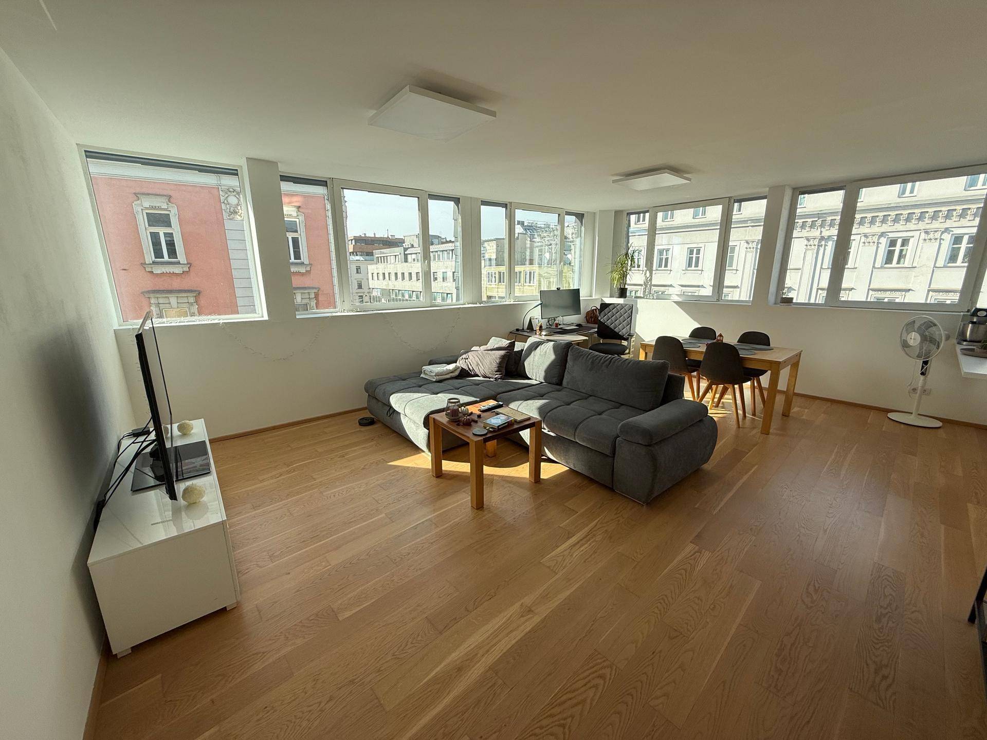 Geräumiger Wohn-Essbereich mit Holzboden, bequemer Couch und Blick auf die Stadt.