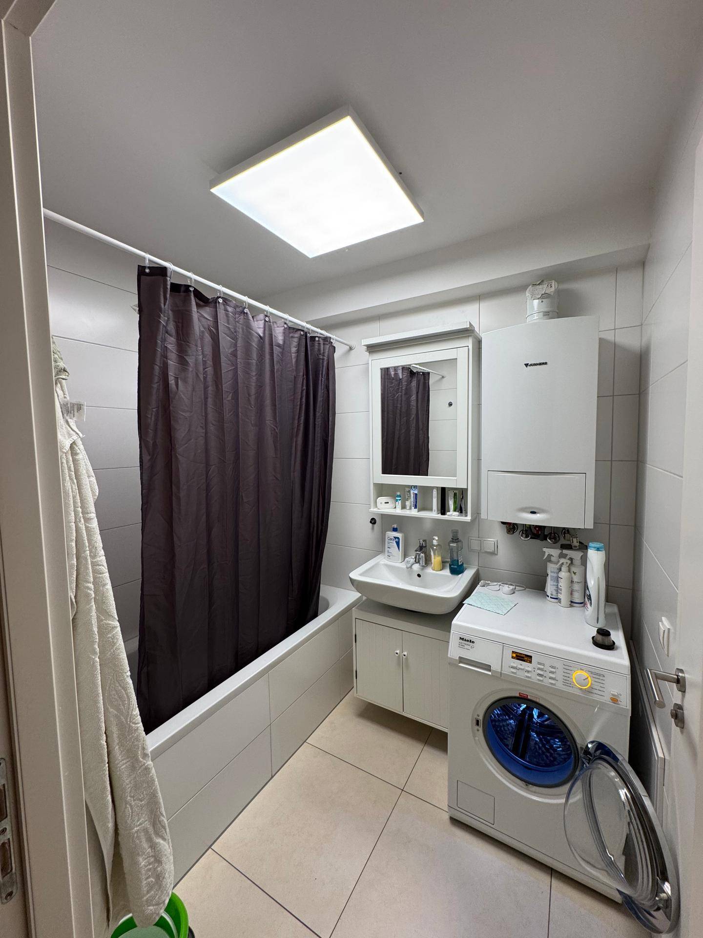 Funktionales Badezimmer mit Badewanne, Waschbecken, Spiegelschrank und Waschmaschine.