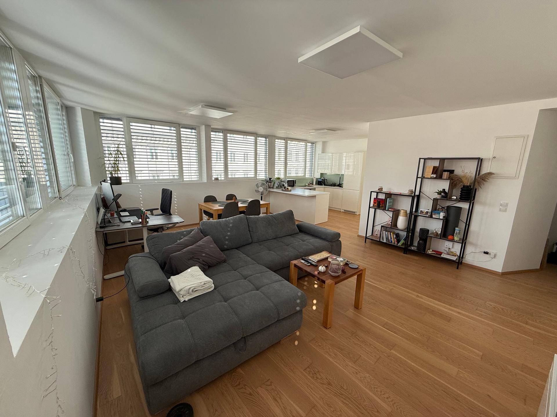 Offener Wohnbereich mit Sofa, Bücherregal und angrenzender Küche, gut beleuchtet.