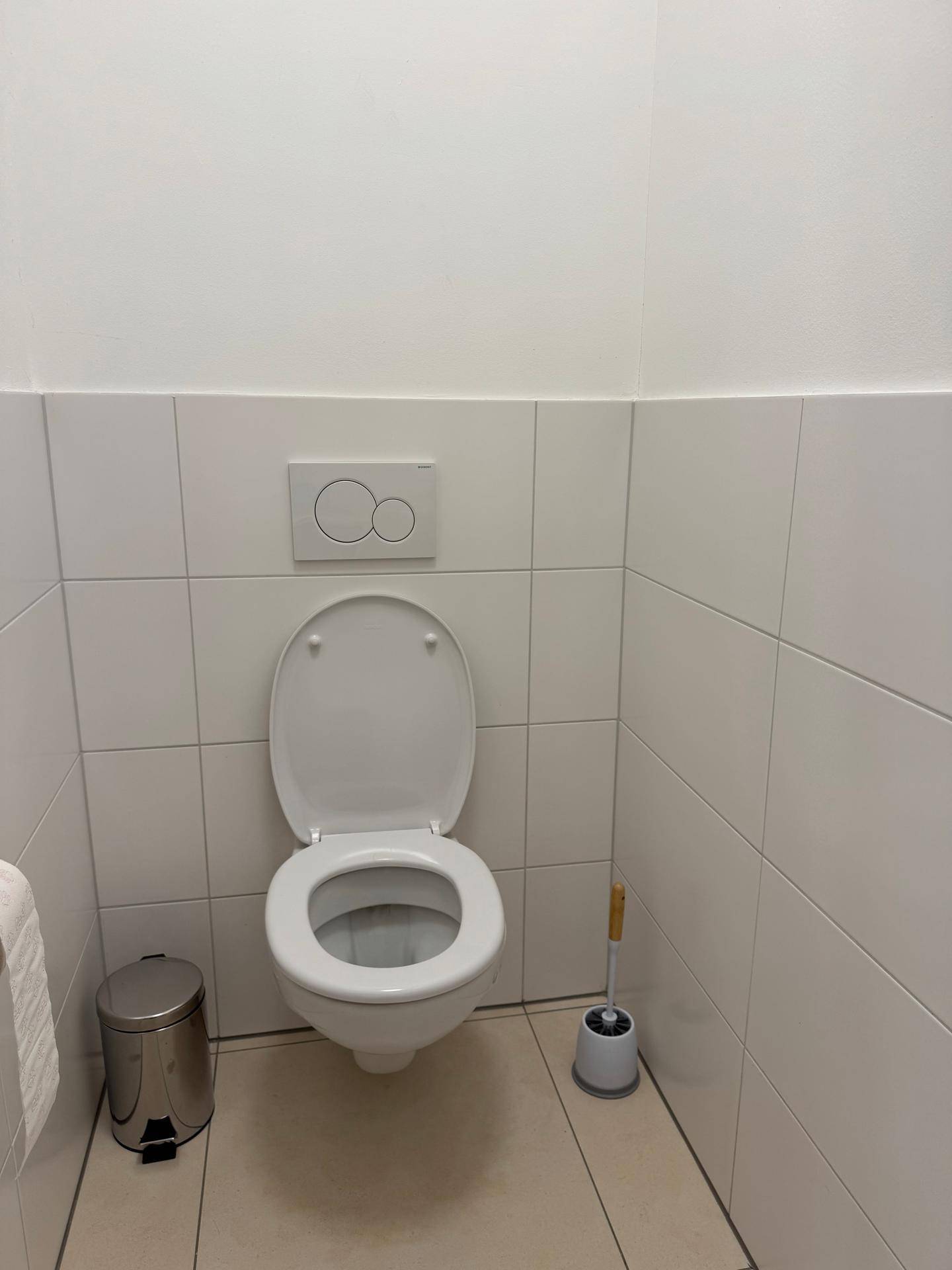 Separates WC mit wandhängender Toilette und Fliesen an Wänden und Boden.