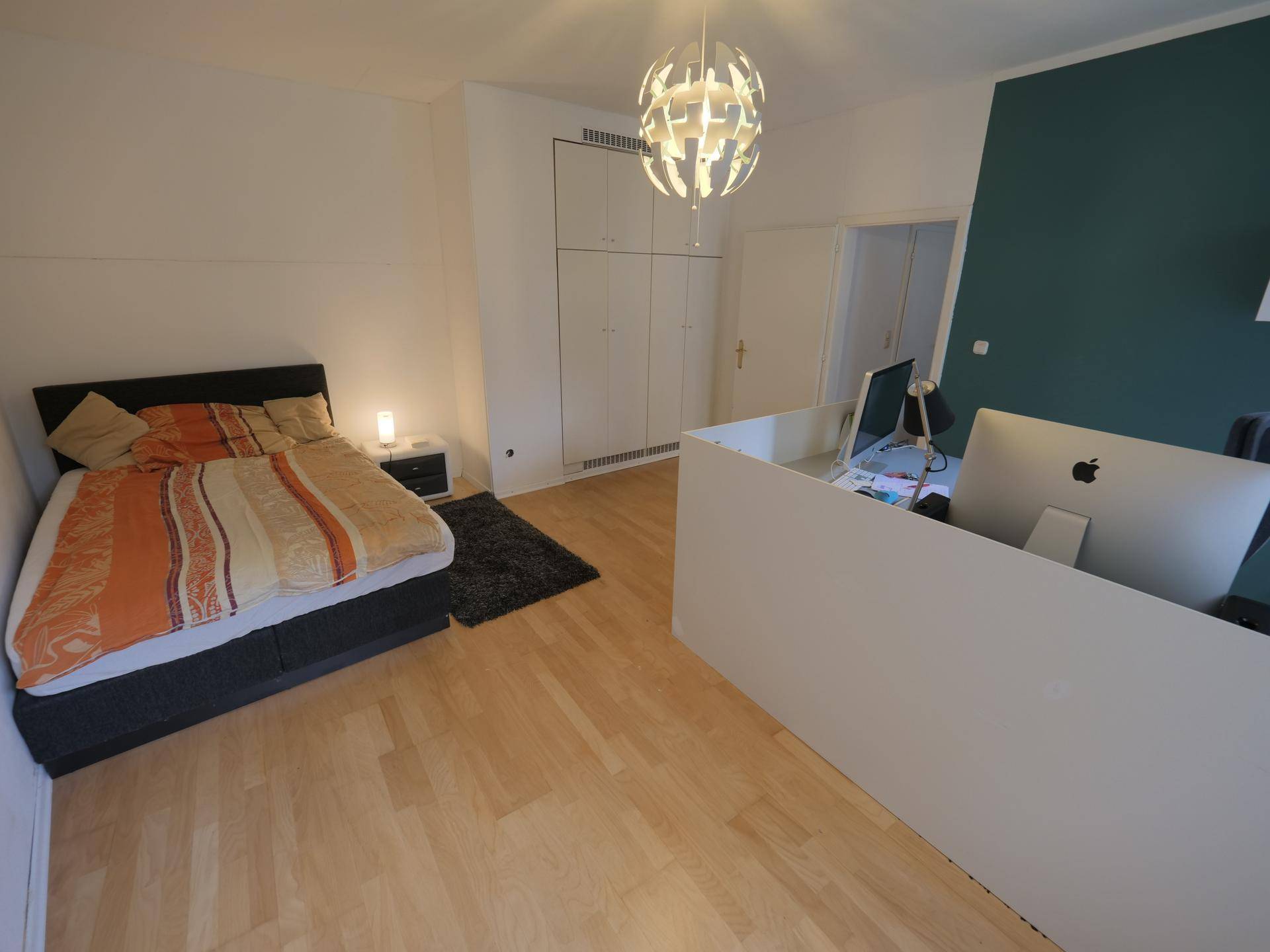 Schlafzimmer mit Bett, Schreibtischbereich und einer farbigen Akzentwand in Dunkelgrün.