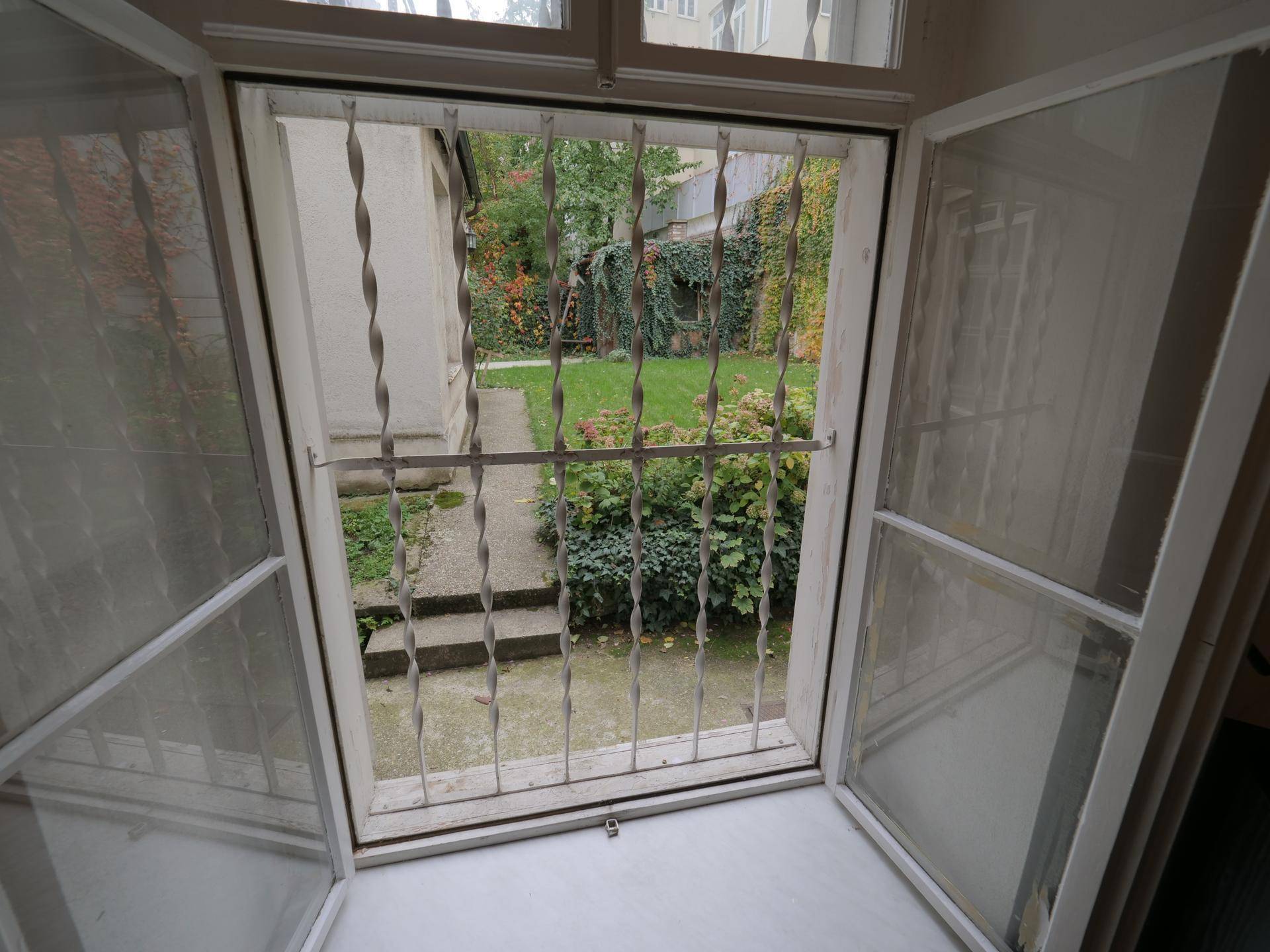 Blick aus dem Fenster in den kleinen, begrünten Gartenbereich mit Treppe und Sicherheitsgittern.