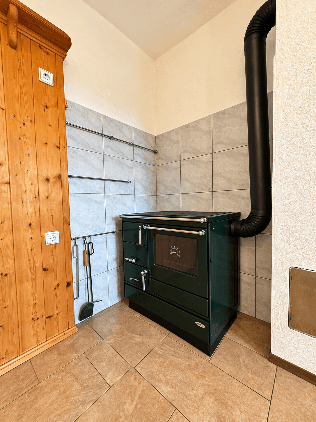 Küchenecke mit traditionellem grünem Holzofen und gefliesten Wänden.