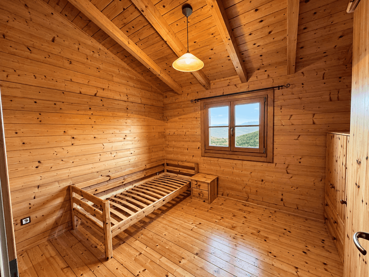 Schlafzimmer mit Holzwänden, Holzboden, Einzelbett und Fenster mit Bergblick.