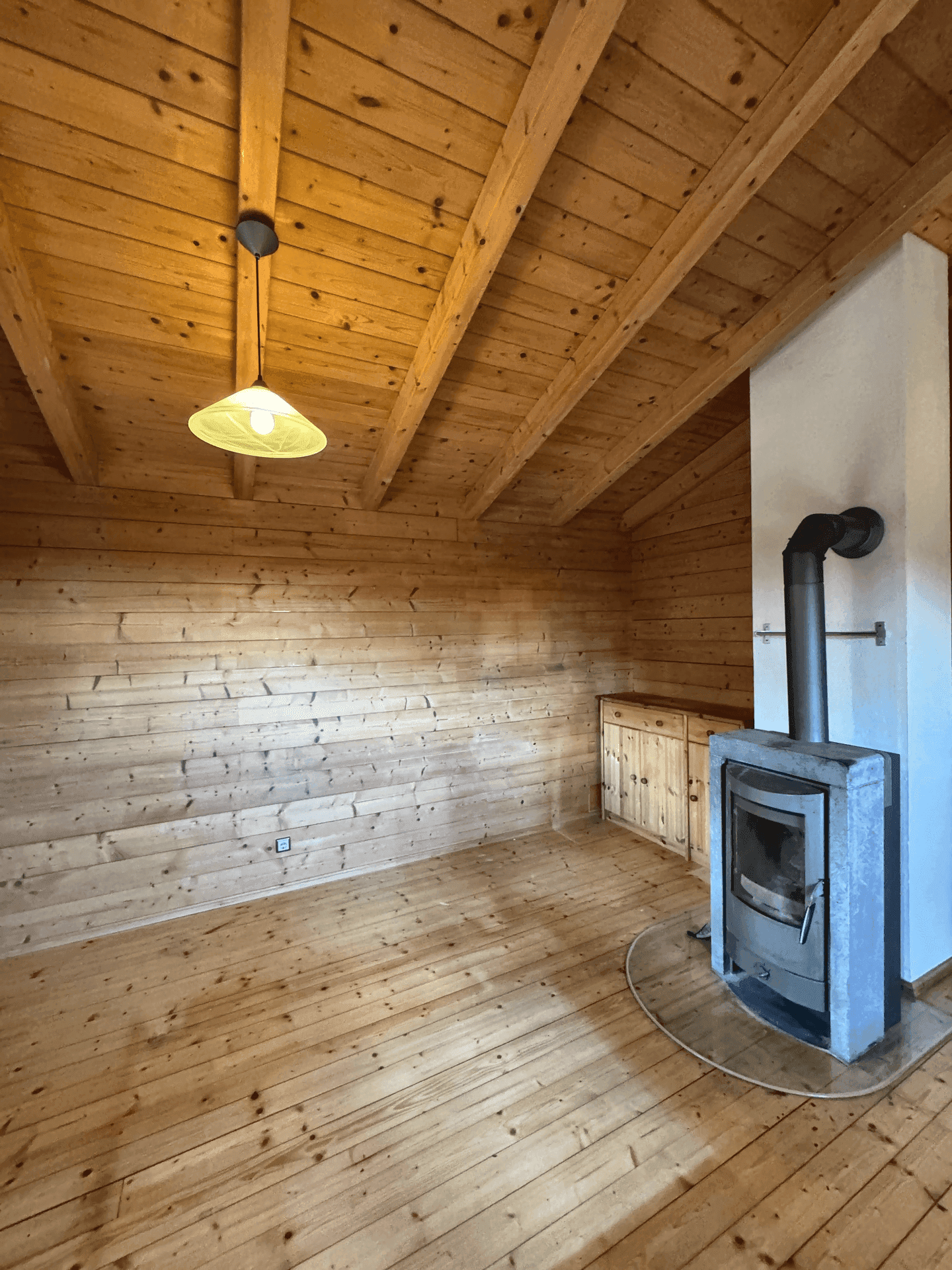 Gemütlicher Raum mit Holzvertäfelung, Holzboden und einem modernen Kaminofen.