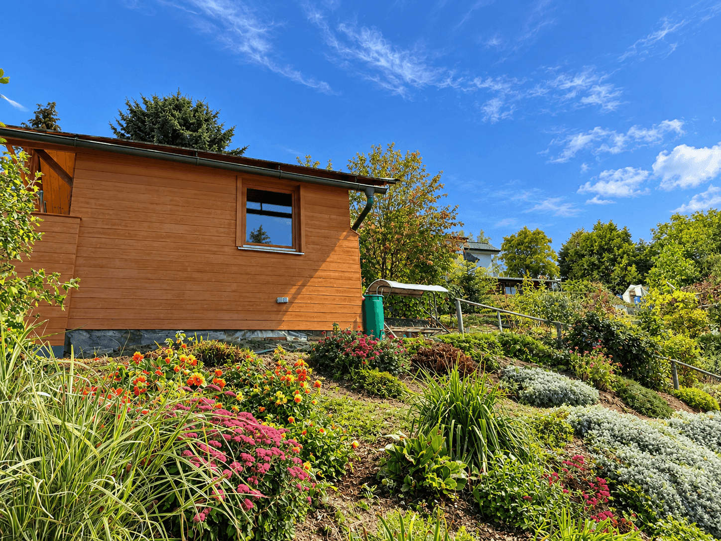 Kleines Holzhaus umgeben von einem blühenden Garten mit verschiedenen Pflanzen.