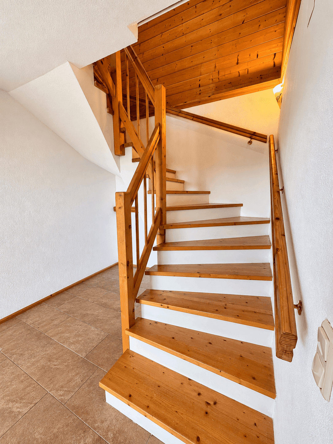 Holztreppe mit weißen Setzstufen und Fliesenboden im Eingangsbereich.