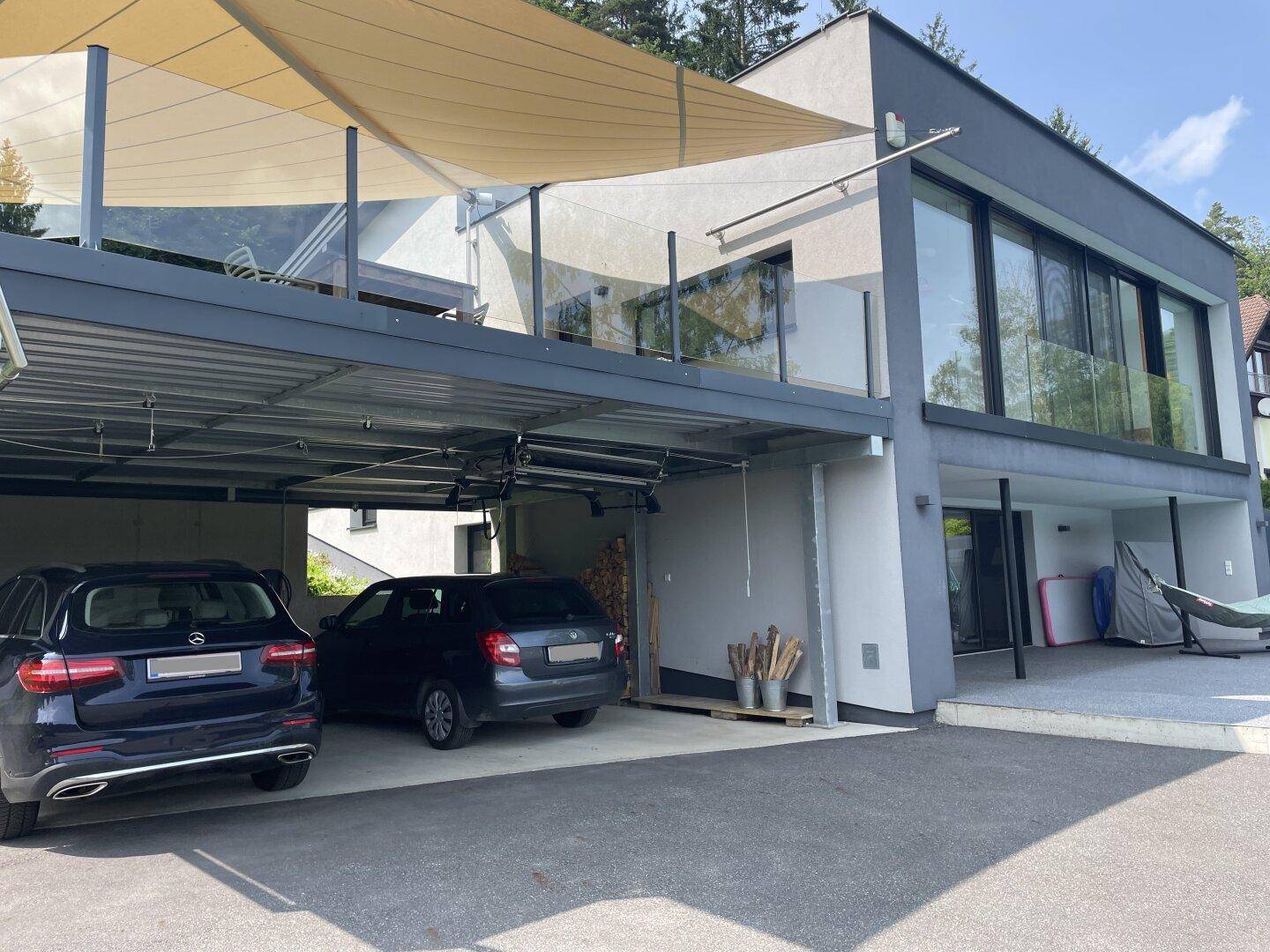Modernes Wohnhaus mit Carport und großer Terrasse, umgeben von Bäumen und mit Blick auf die Natur.