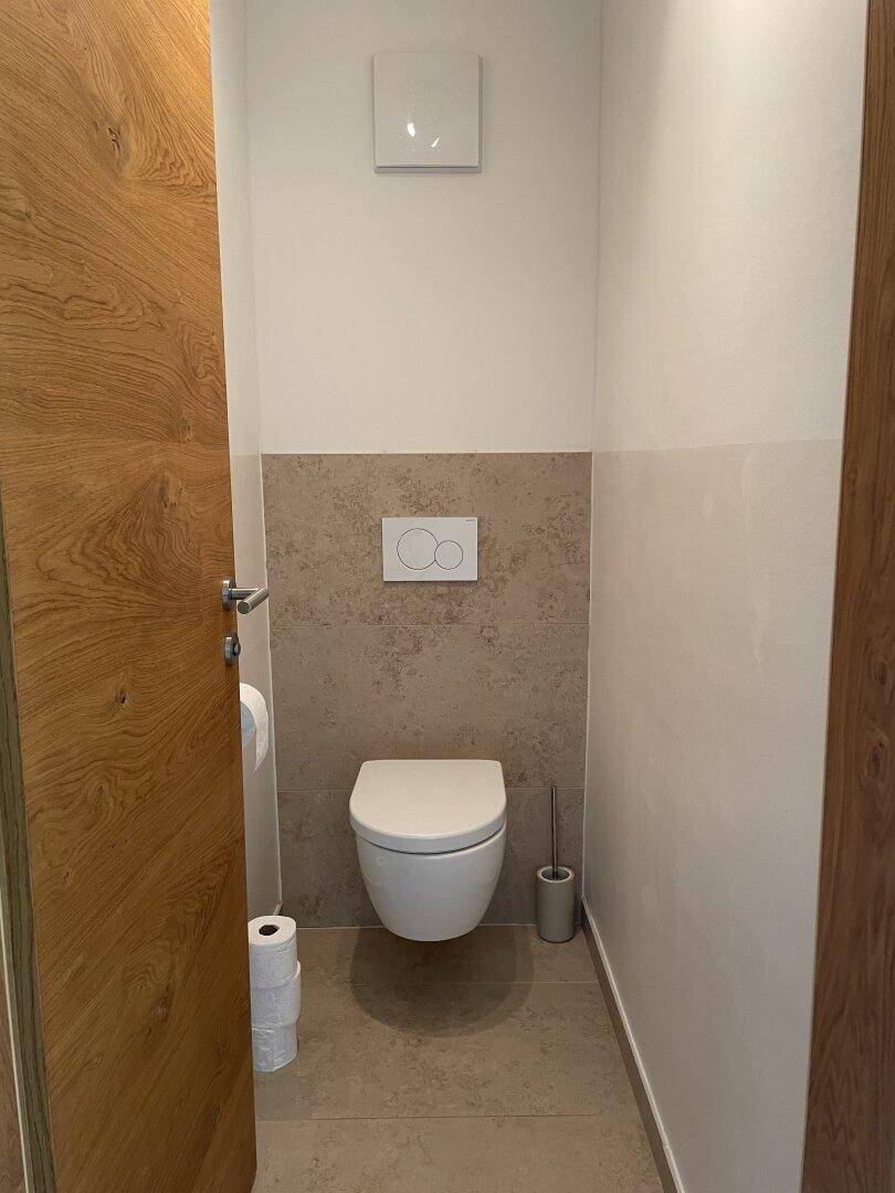 Separates Gäste-WC mit wandhängender Toilette und modernen Fliesen, schlicht und funktional gestaltet.