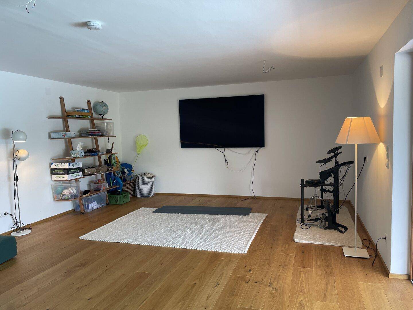 Helles Wohnzimmer mit Holzboden, großem Fernseher und Stehlampe, ideal für Unterhaltung.