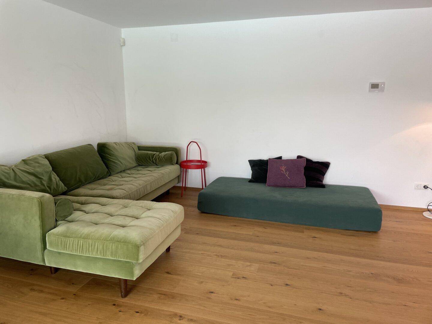 Gemütliches Wohnzimmer mit grünem Ecksofa und Holzboden, einladend zum Entspannen.