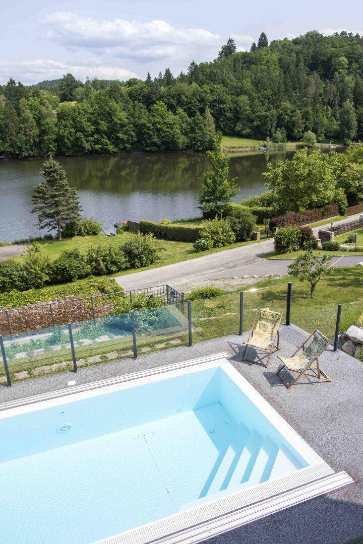 Außenpool mit weitem Blick auf den See und die umliegende Landschaft, umgeben von Grünflächen.