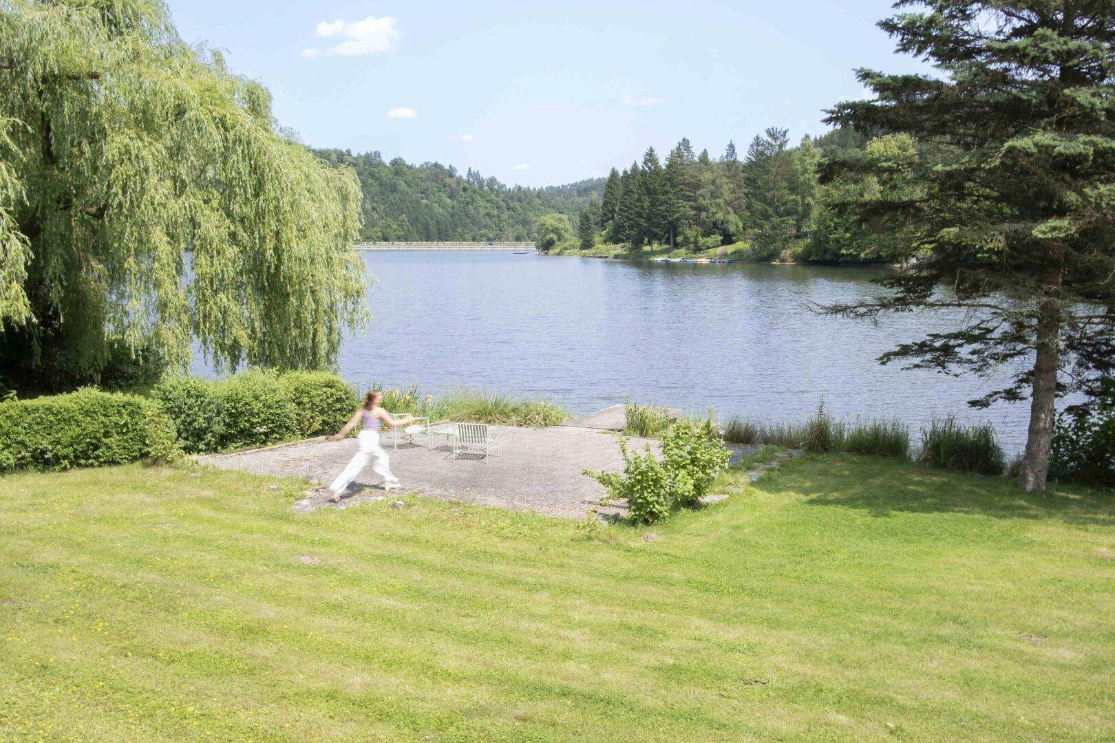 Gepflegter Gartenbereich mit Rasenfläche und kleiner Terrasse direkt am Seeufer, umgeben von üppigem Grün.