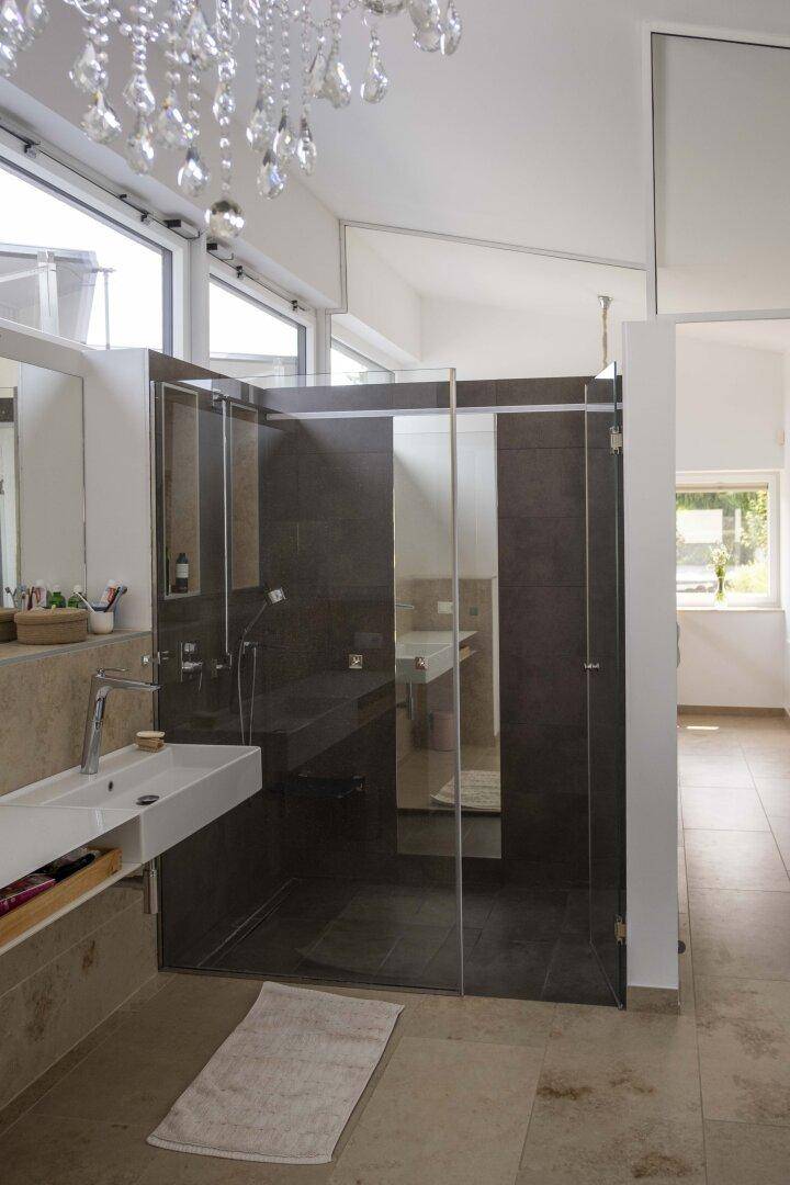Modernes Badezimmer mit begehbarer Dusche, Doppelwaschbecken und eleganten dunklen Fliesen.