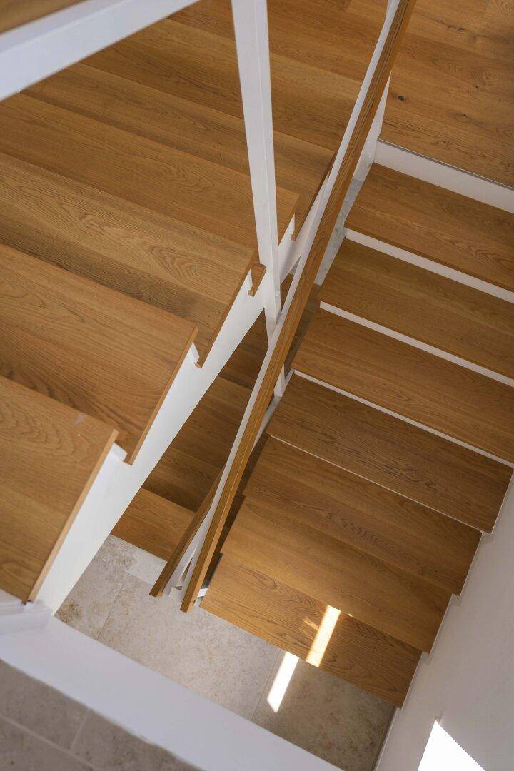 Moderne Holztreppe mit weißem Geländer, die verschiedene Ebenen des Hauses miteinander verbindet.