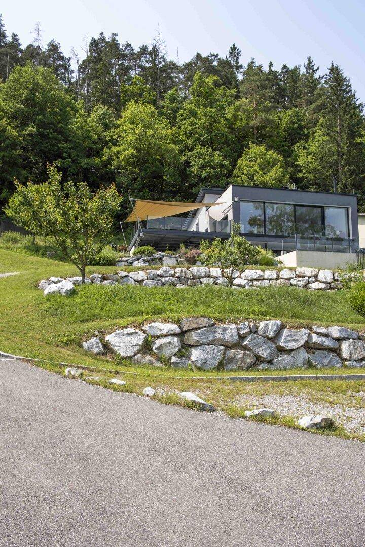 Modernes Haus in Hanglage mit großen Fenstern und Terrassen, umgeben von Wald und Felsen.