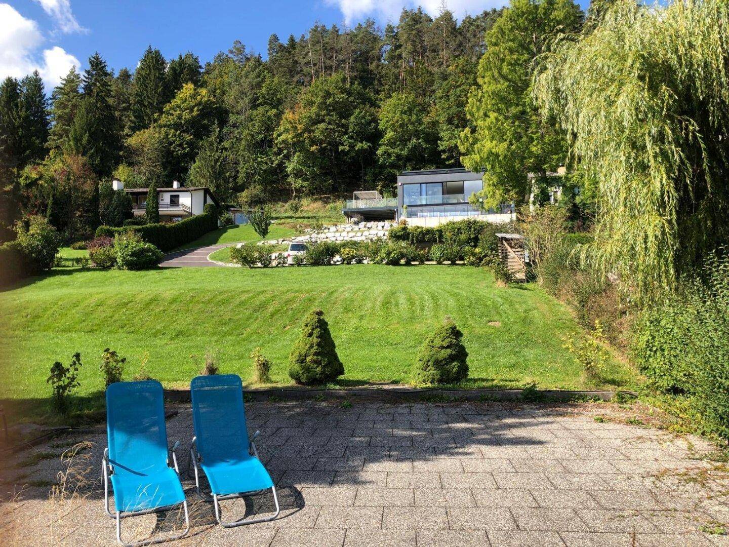 Gepflasterte Terrasse mit Liegestühlen und weitem Blick auf den Garten und die umliegende Natur.