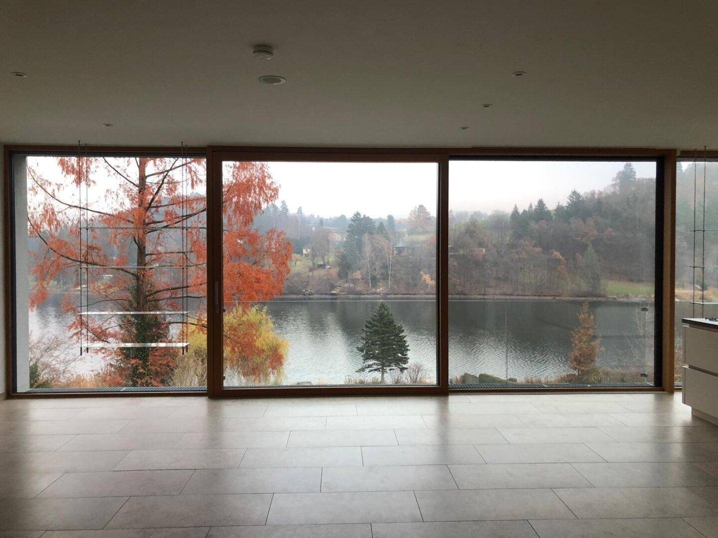 Geräumiger Wohnbereich mit großen Panoramafenstern, die einen beeindruckenden Blick auf den See und die Natur freigeben.