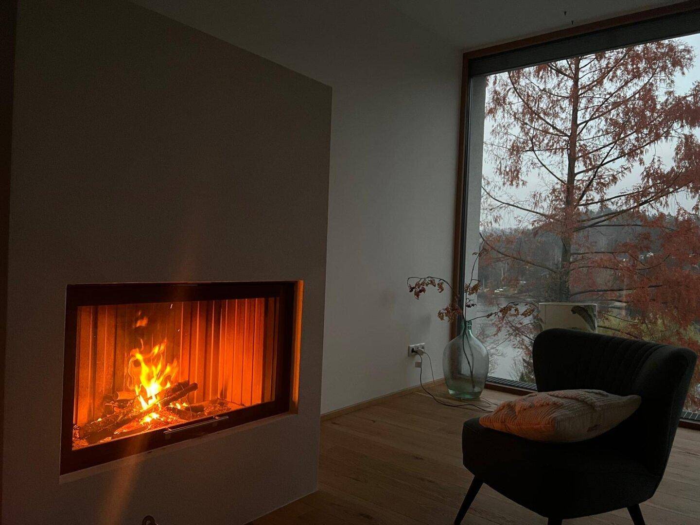Gemütliches Wohnzimmer mit Kamin und großem Fenster, das einen malerischen Blick auf den See bietet.