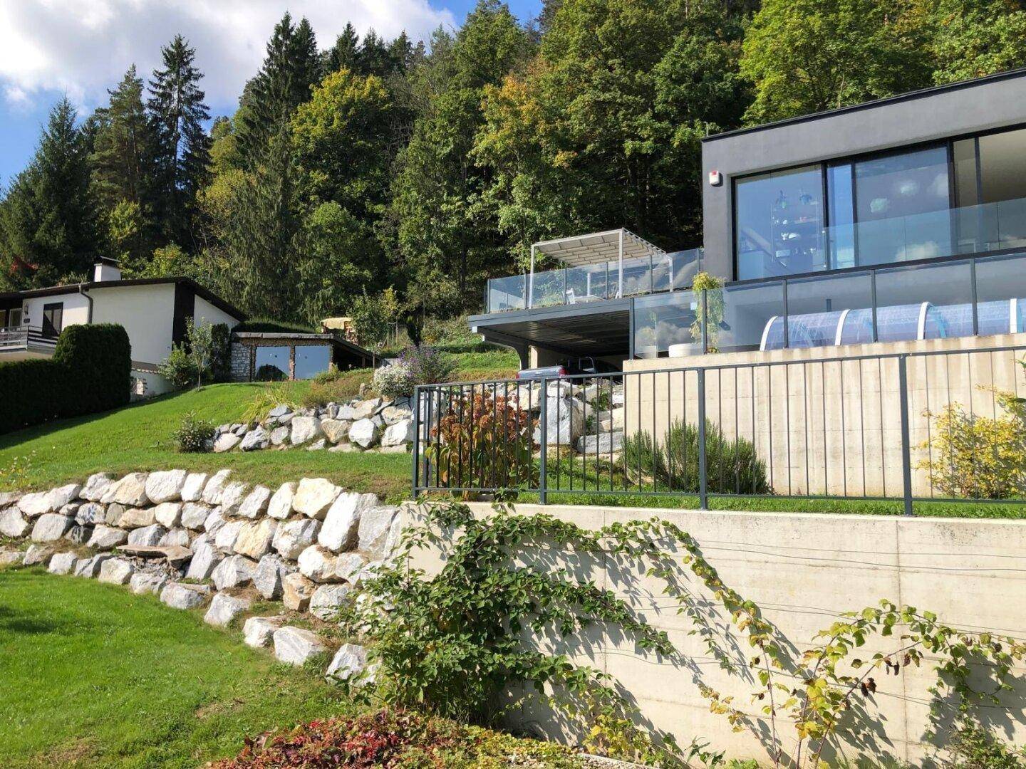 Modernes Haus in Hanglage mit Terrassen und Garten, umgeben von Wald und Felsen.