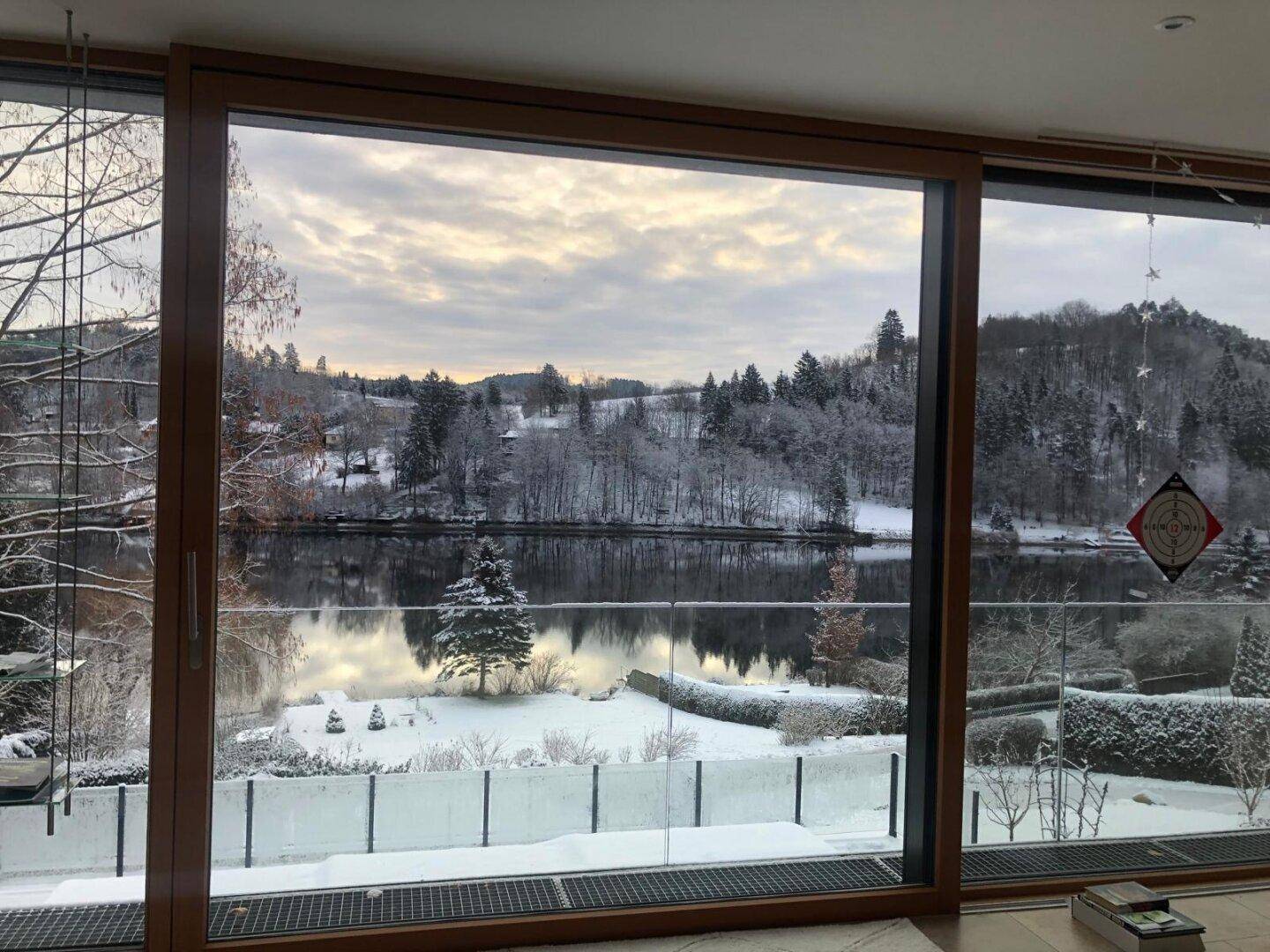 Winterlicher Ausblick aus dem Wohnzimmer auf den verschneiten See und die Umgebung, eine malerische Szene.