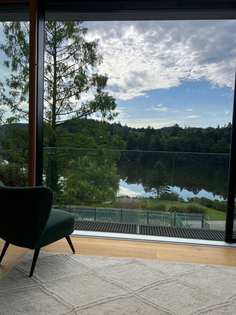 Heller Wohnbereich mit großem Fenster und Blick auf den See und die Natur, einladend und offen.