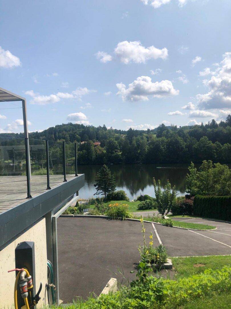 Terrasse mit Glasgeländer und weitem Blick auf den See und die bewaldete Umgebung.