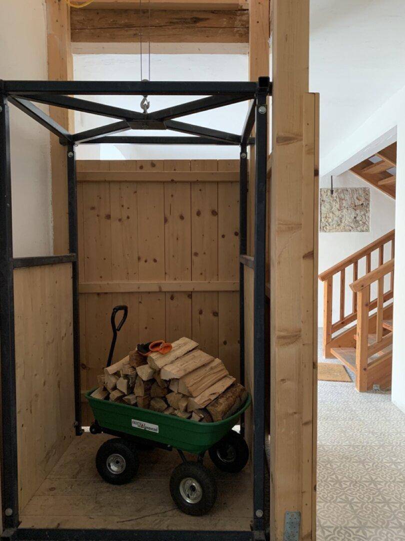 Lagerbereich mit einem Holzaufzug und gestapeltem Brennholz.