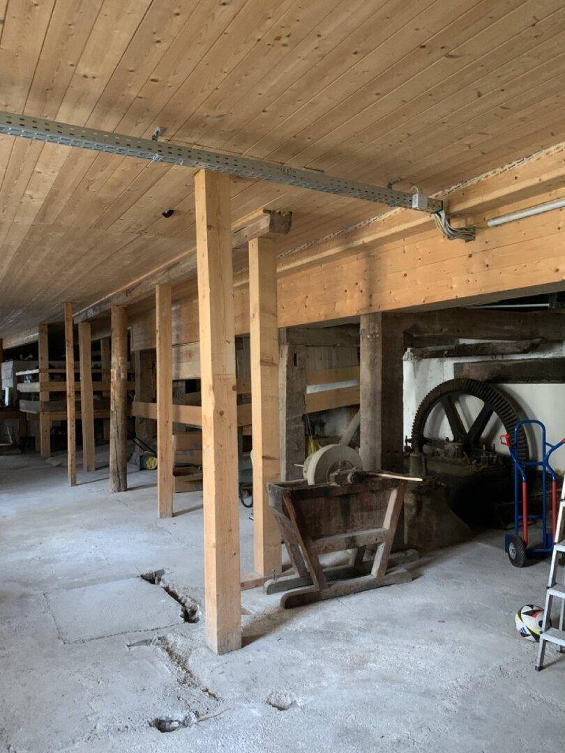 Geräumiger Werkstattbereich mit Holzbalken, Betonboden und alten Maschinenteilen.