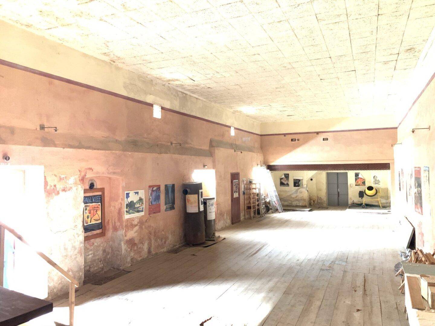 Großer, leerer Saal mit Holzboden und hohen Decken, möglicherweise für Veranstaltungen.