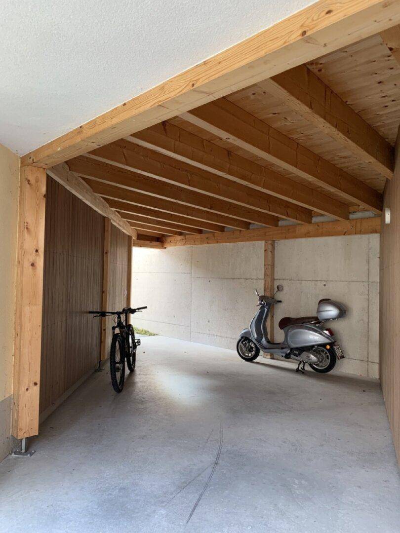 Überdachter Parkplatz mit Holzbalkenkonstruktion für Fahrräder und Roller.