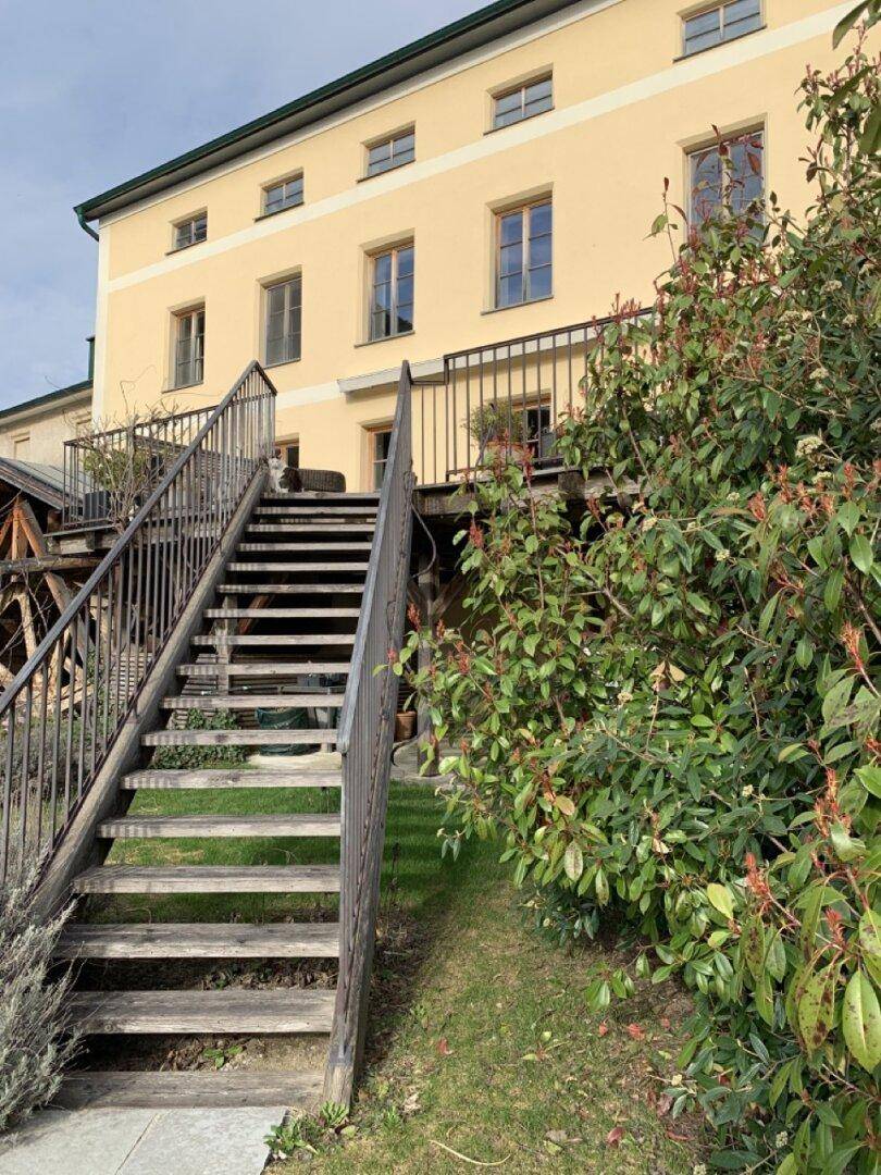 Außentreppe führt zu einer oberen Etage des historischen Gebäudes mit grüner Bepflanzung.