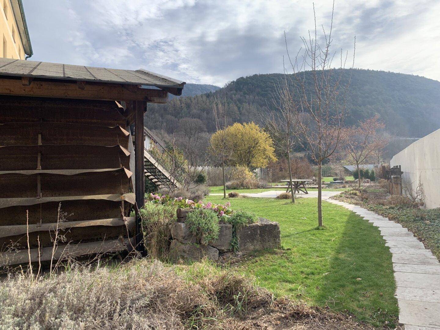 Gartenweg führt durch eine grüne Landschaft mit Bäumen und einem historischen Gebäude.