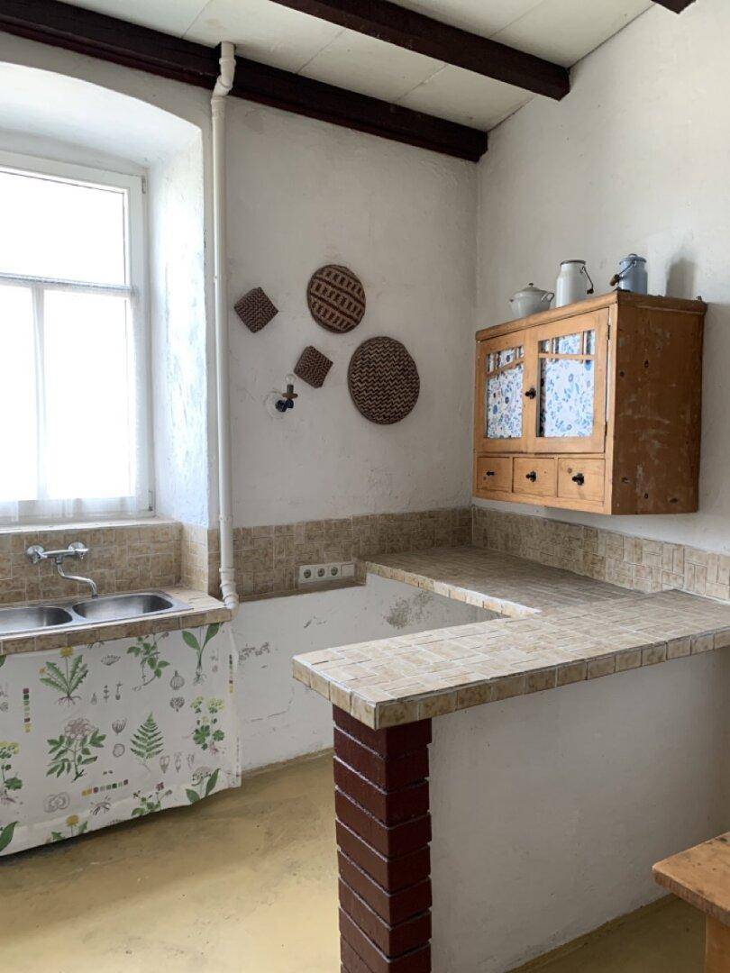 Einfache Küche mit gefliesten Arbeitsflächen, Spüle und einem Holzschrank.