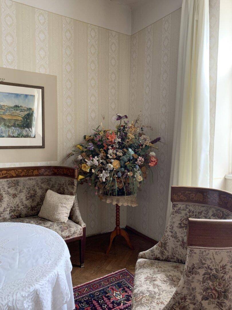 Klassisch eingerichteter Raum mit gemusterten Tapeten, antiken Möbeln und Blumenarrangement.