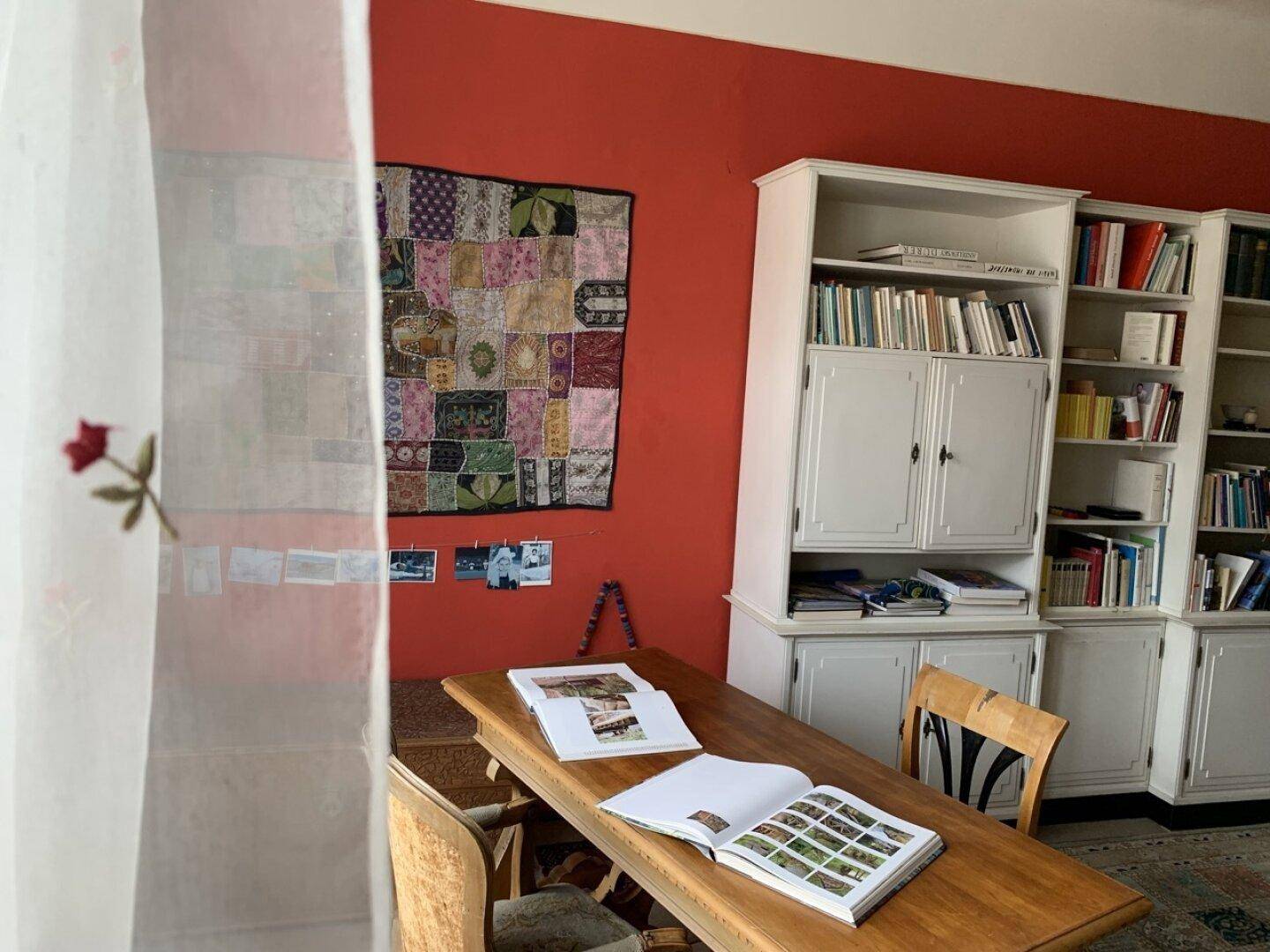 Arbeitsbereich mit Bücherregalen, Holztisch und einer roten Akzentwand.