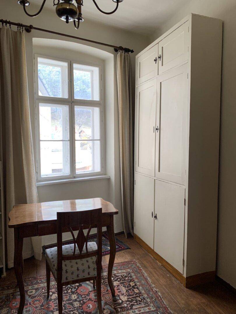 Kleines Arbeitszimmer mit Holztisch, Schrank und Fenster.