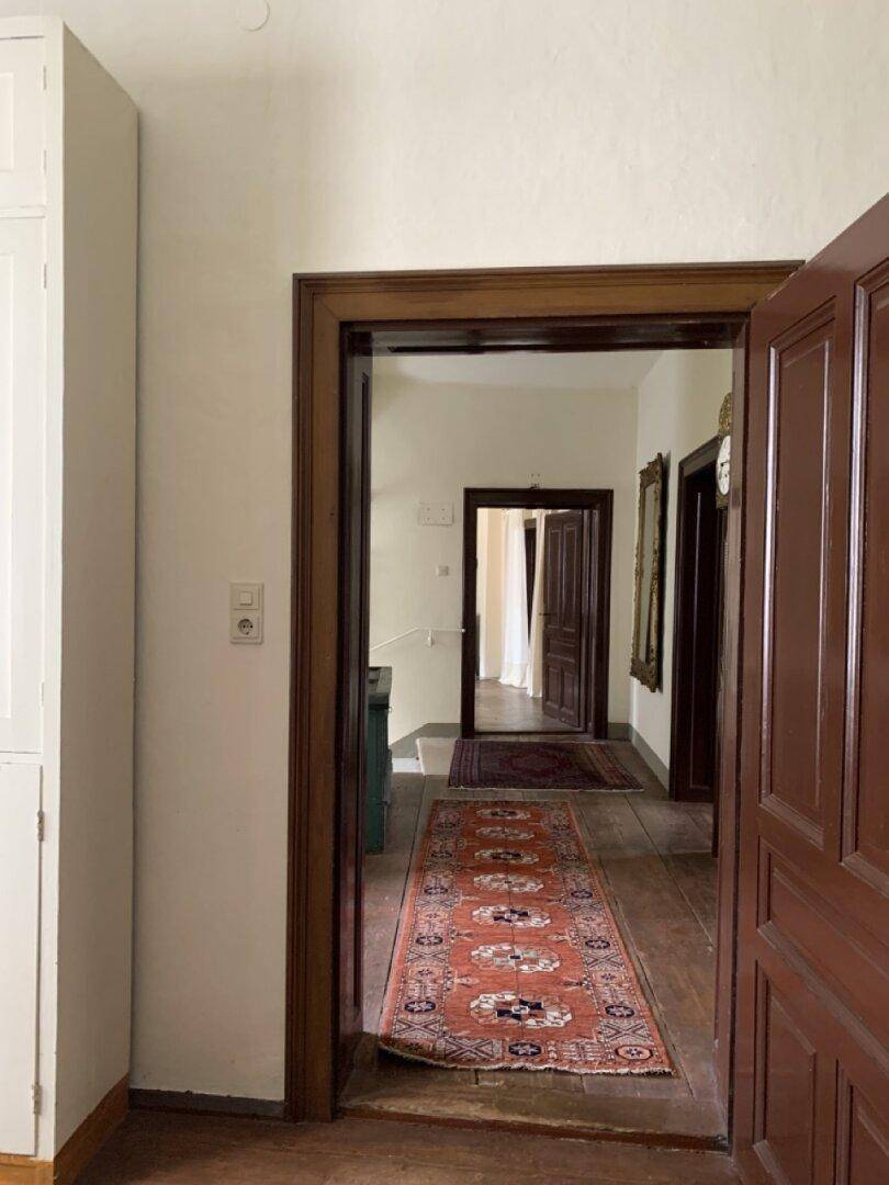 Langer Flur mit Holztüren, Teppichen und Blick in weitere Räume.